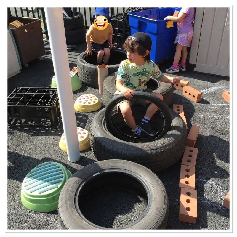 Child playing with tyres and loose parts outdoors, Ysgol Feithrin Y Trallwng, Welshpool